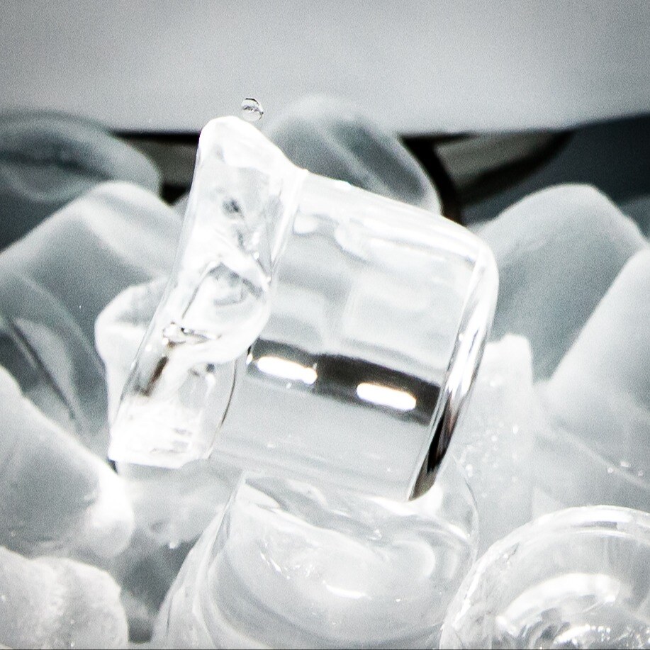 A close-up of transparent ice cubes with smooth and jagged edges, glistening under bright light.