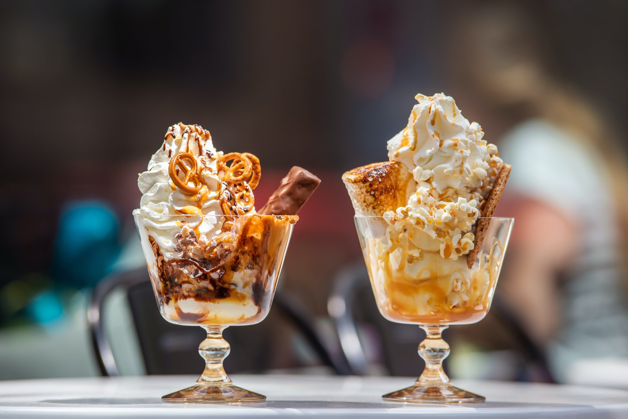Two gourmet sundaes in elegant glass cups, one topped with pretzels, chocolate, and caramel, the other with popcorn, toasted marshmallow, and caramel drizzle.